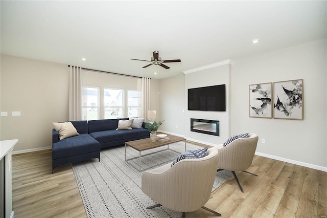 living area with light wood-style floors, a glass covered fireplace, ceiling fan, baseboards, and recessed lighting
