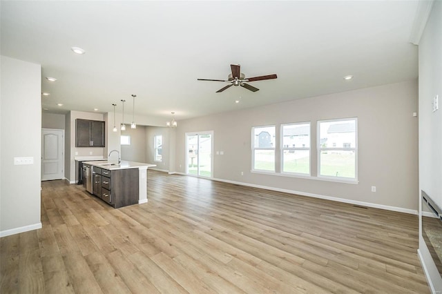 kitchen featuring a sink, light countertops, open floor plan, baseboards, and light wood-style flooring