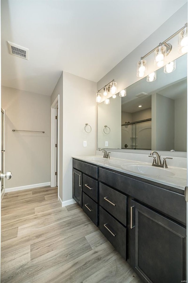 bathroom with an enclosed shower, wood finished floors, double vanity, and baseboards