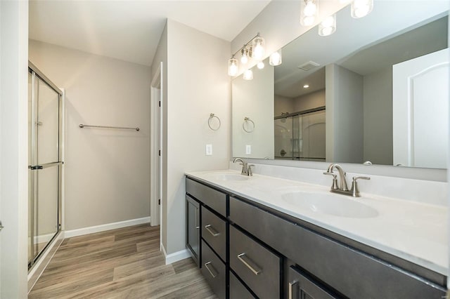 bathroom featuring wood finished floors, a stall shower, baseboards, and double vanity