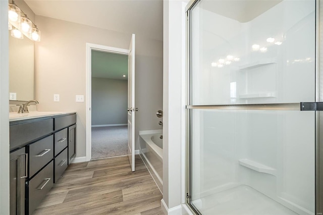 bathroom with a shower with shower door, wood finished floors, double vanity, and a garden tub