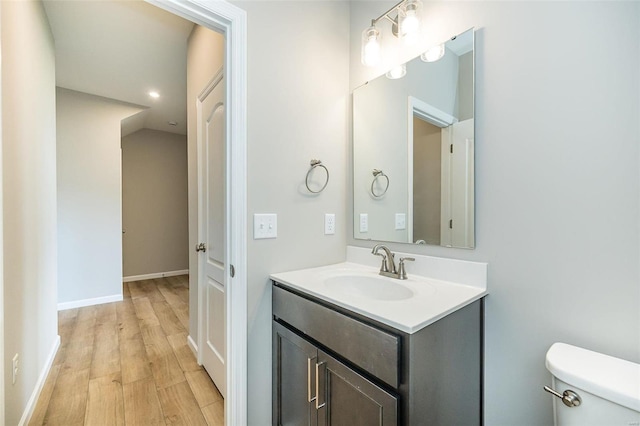 bathroom with wood finished floors, toilet, vanity, and baseboards