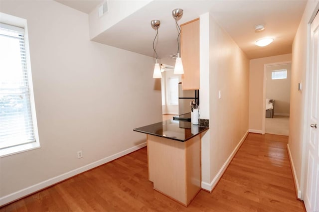 kitchen with light wood-type flooring, freestanding refrigerator, dark countertops, and a peninsula