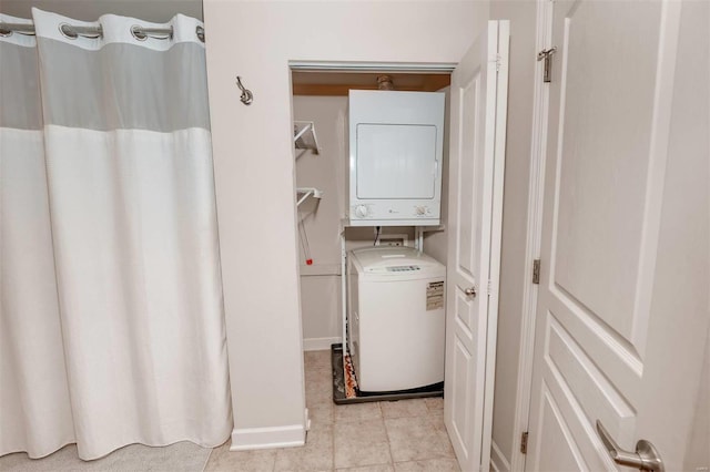 laundry room with stacked washing machine and dryer, light tile patterned flooring, and baseboards