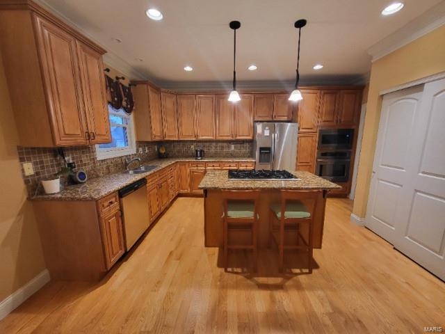 kitchen featuring stainless steel appliances, brown cabinetry, a kitchen island, light wood finished floors, and light stone countertops