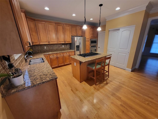 kitchen with stainless steel appliances, a sink, crown molding, a center island, and brown cabinets