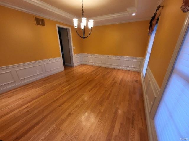 unfurnished room featuring a raised ceiling, crown molding, a chandelier, a decorative wall, and light wood-style floors