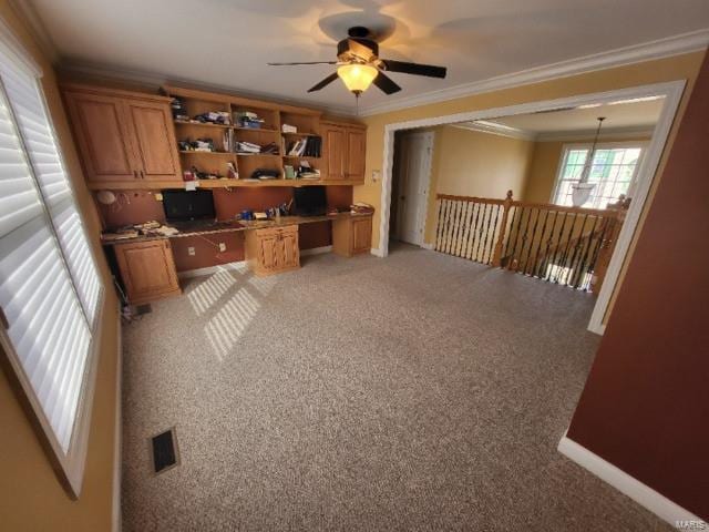 unfurnished office featuring built in study area, a ceiling fan, crown molding, light colored carpet, and baseboards