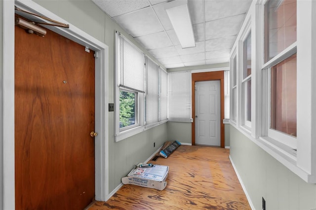 doorway to outside featuring a paneled ceiling, baseboards, and wood finished floors
