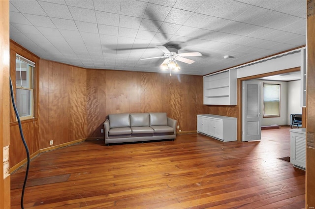 unfurnished room with wood-type flooring, a ceiling fan, wood walls, and baseboards