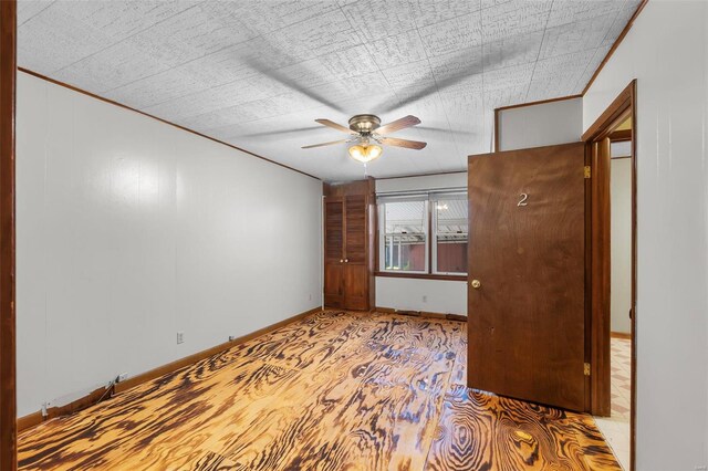 unfurnished bedroom with ornamental molding, a ceiling fan, baseboards, and wood finished floors