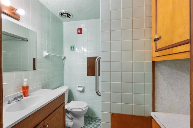 bathroom with tile walls, vanity, a tile shower, and toilet