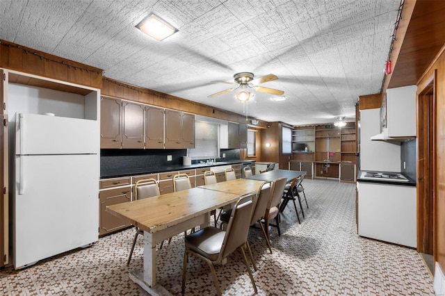 kitchen featuring freestanding refrigerator, dark countertops, a ceiling fan, light floors, and stainless steel cooktop