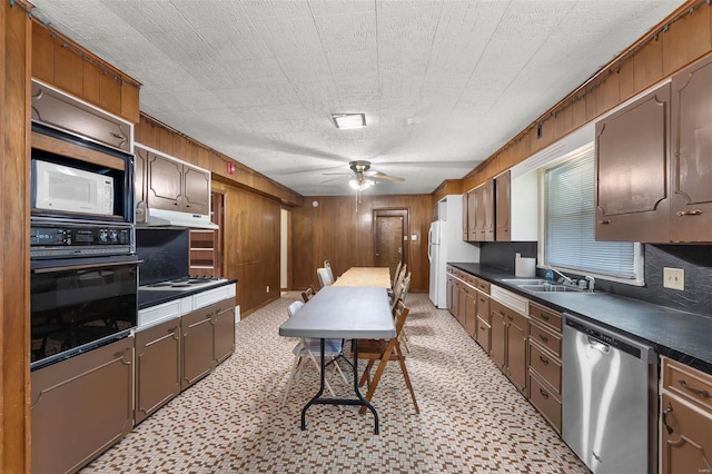 kitchen with white appliances, a sink, dark countertops, a ceiling fan, and wood walls