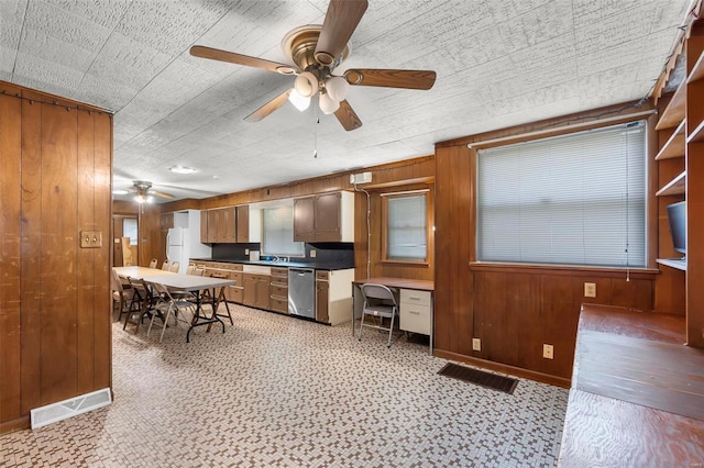 kitchen featuring dishwasher, a ceiling fan, wooden walls, freestanding refrigerator, and light floors