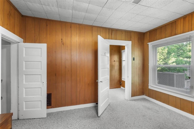 spare room featuring light carpet, wooden walls, and baseboards