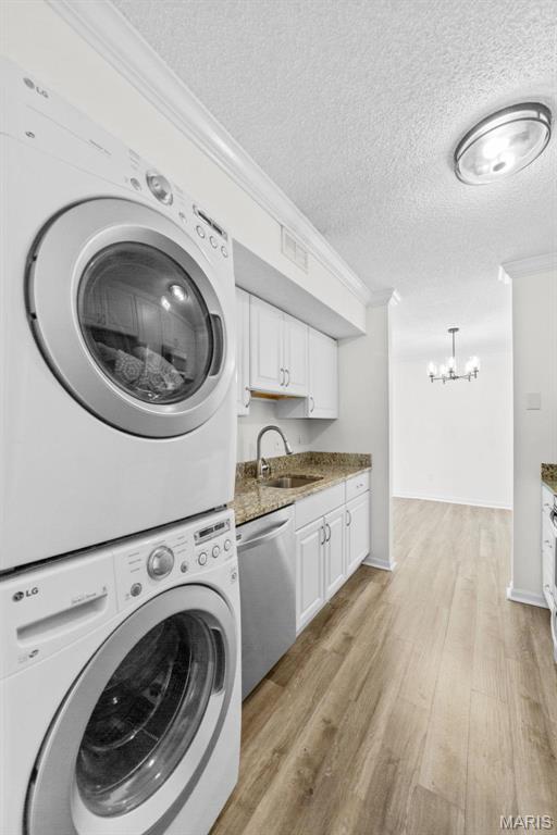 1509 Swallow Dr, Saint Louis, MO 63144 - laundry room featuring stacked washing machine and dryer, ornamental molding, a chandelier, a textured ceiling, and light wood-type flooring