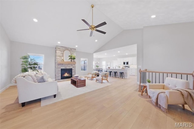 living area featuring light wood-style floors, a ceiling fan, a fireplace, high vaulted ceiling, and recessed lighting