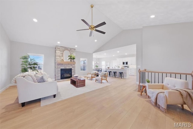 living room with light wood-style floors, ceiling fan, a stone fireplace, high vaulted ceiling, and recessed lighting