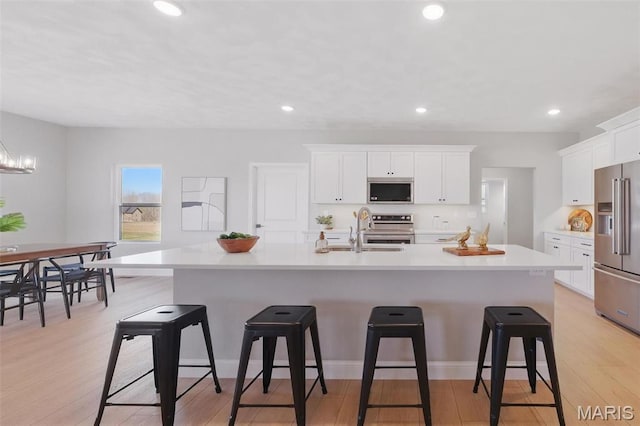 kitchen with appliances with stainless steel finishes, a sink, white cabinets, a kitchen bar, and light countertops