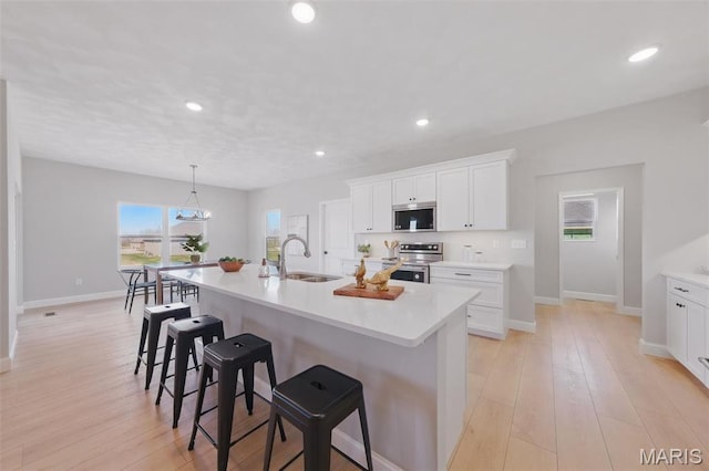 kitchen featuring stainless steel appliances, a sink, a breakfast bar, light countertops, and an island with sink