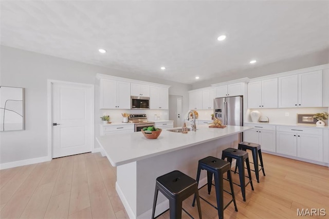 kitchen with appliances with stainless steel finishes, a sink, a breakfast bar area, a center island with sink, and white cabinets