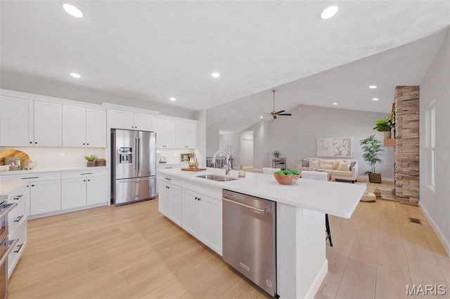 kitchen featuring stainless steel appliances, a sink, a kitchen island with sink, ceiling fan, and white cabinetry