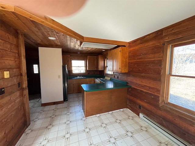 kitchen with freestanding refrigerator, wooden walls, baseboard heating, a peninsula, and light floors