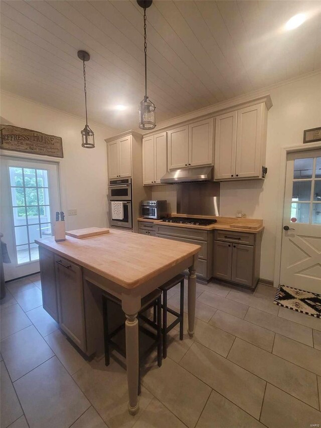 kitchen with under cabinet range hood, cooktop, hanging light fixtures, ornamental molding, and light tile patterned floors
