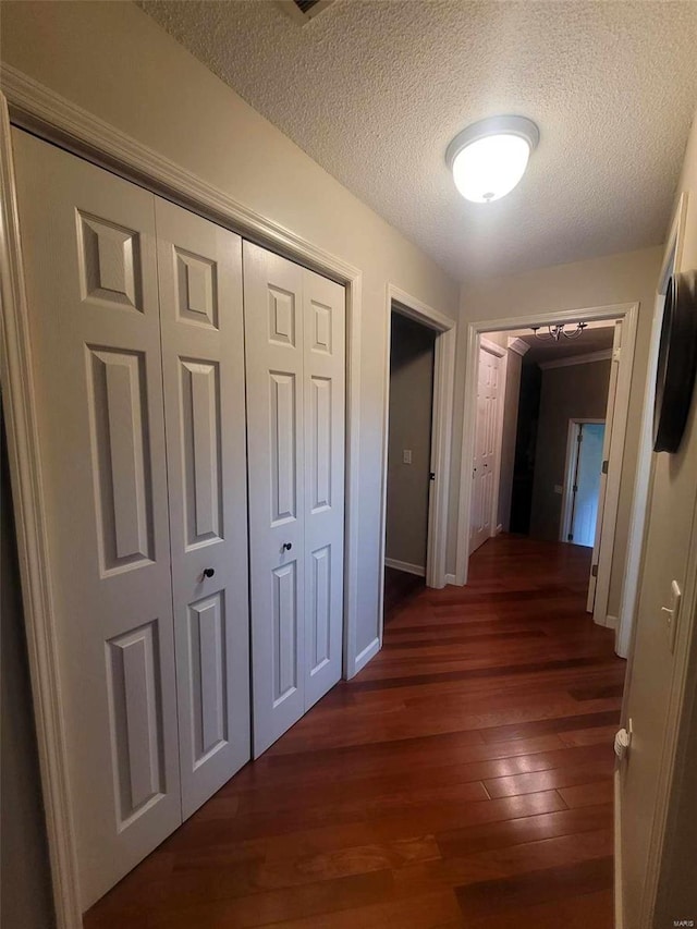 hall with dark wood-type flooring, a textured ceiling, and baseboards