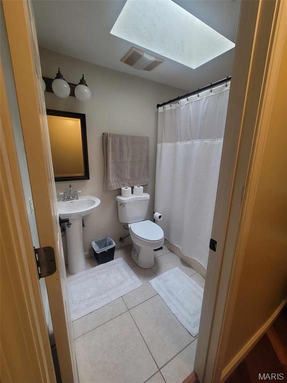 16225 Shady Ln, Dexter, MO 63841 - full bathroom featuring tile patterned floors, toilet, a skylight, a sink, and curtained shower