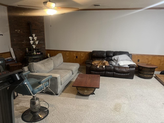 carpeted living area featuring a wood stove, a wainscoted wall, ceiling fan, and wooden walls