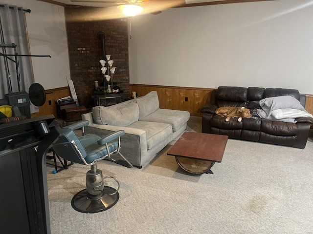 living room with carpet, wainscoting, a wood stove, ceiling fan, and wooden walls