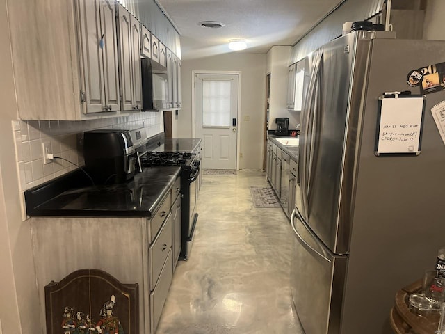 kitchen with freestanding refrigerator, gas stove, backsplash, dark countertops, and concrete floors