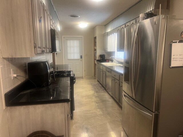 kitchen featuring stainless steel appliances, decorative backsplash, a sink, dark countertops, and finished concrete flooring