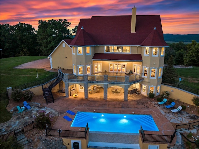 back of house at dusk with stairs, stucco siding, a balcony, and a patio