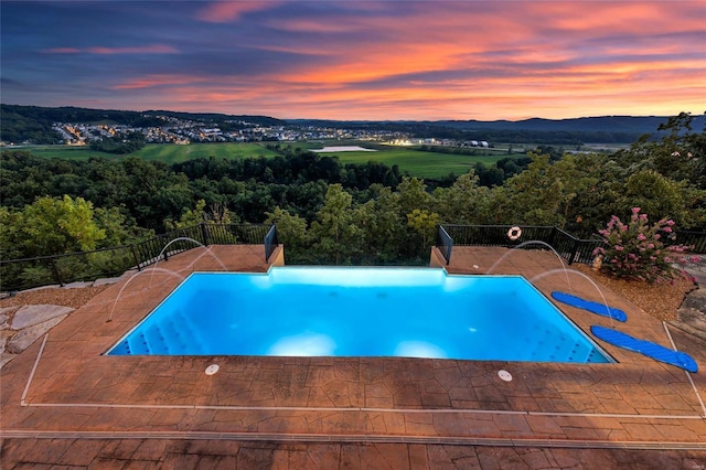 pool at dusk featuring fence and a patio area