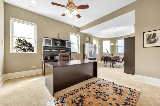 office area featuring light colored carpet, ceiling fan, baseboards, a raised ceiling, and a chandelier