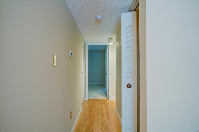 hall with light wood-style floors, baseboards, and a textured ceiling