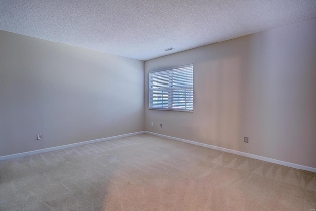 spare room featuring light colored carpet, a textured ceiling, and baseboards