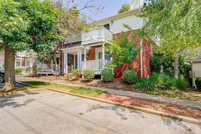 view of front of property with brick siding, a balcony, a porch, and uncovered parking