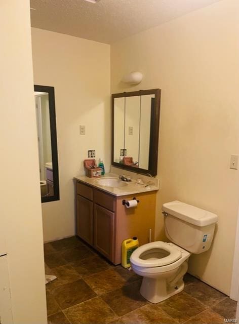 bathroom featuring vanity, toilet, a textured ceiling, and stone finish floors