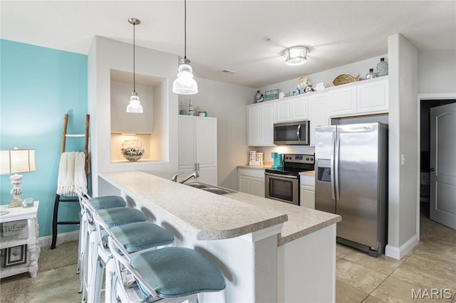 kitchen with stainless steel appliances, a sink, light countertops, a kitchen bar, and white cabinets