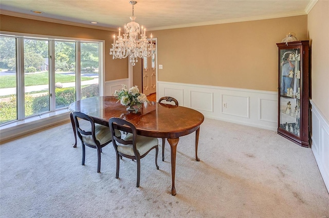 dining area with a chandelier, carpet, a wainscoted wall, crown molding, and a decorative wall