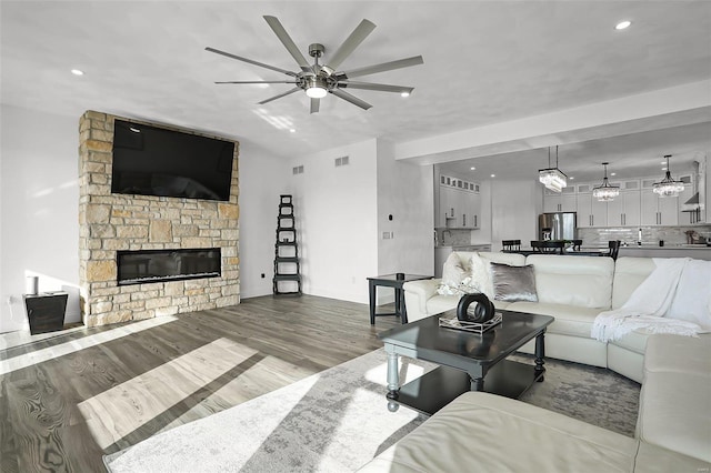 living room with a ceiling fan, wood finished floors, a stone fireplace, baseboards, and recessed lighting