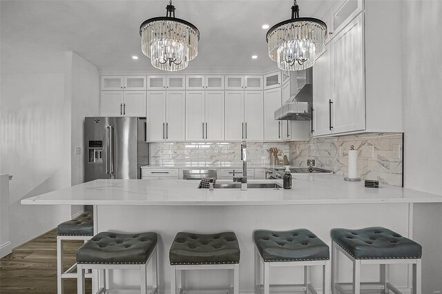 kitchen with a chandelier, high end refrigerator, wall chimney range hood, a peninsula, and recessed lighting