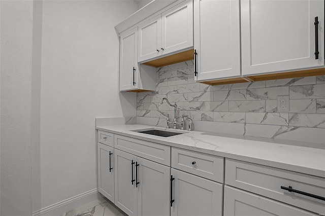 kitchen with a sink, light marble finish floors, decorative backsplash, and white cabinets