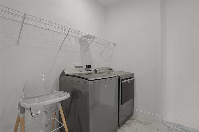 washroom featuring washing machine and clothes dryer, baseboards, and light marble finish floors