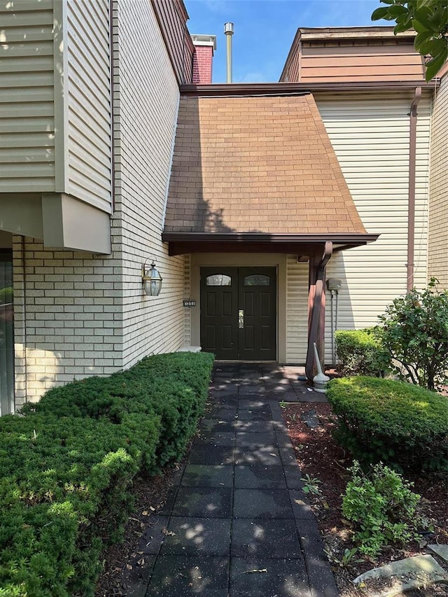 property entrance featuring brick siding, a chimney, and roof with shingles