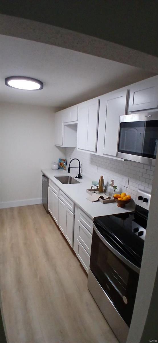kitchen featuring stainless steel appliances, a sink, backsplash, and light wood-style flooring